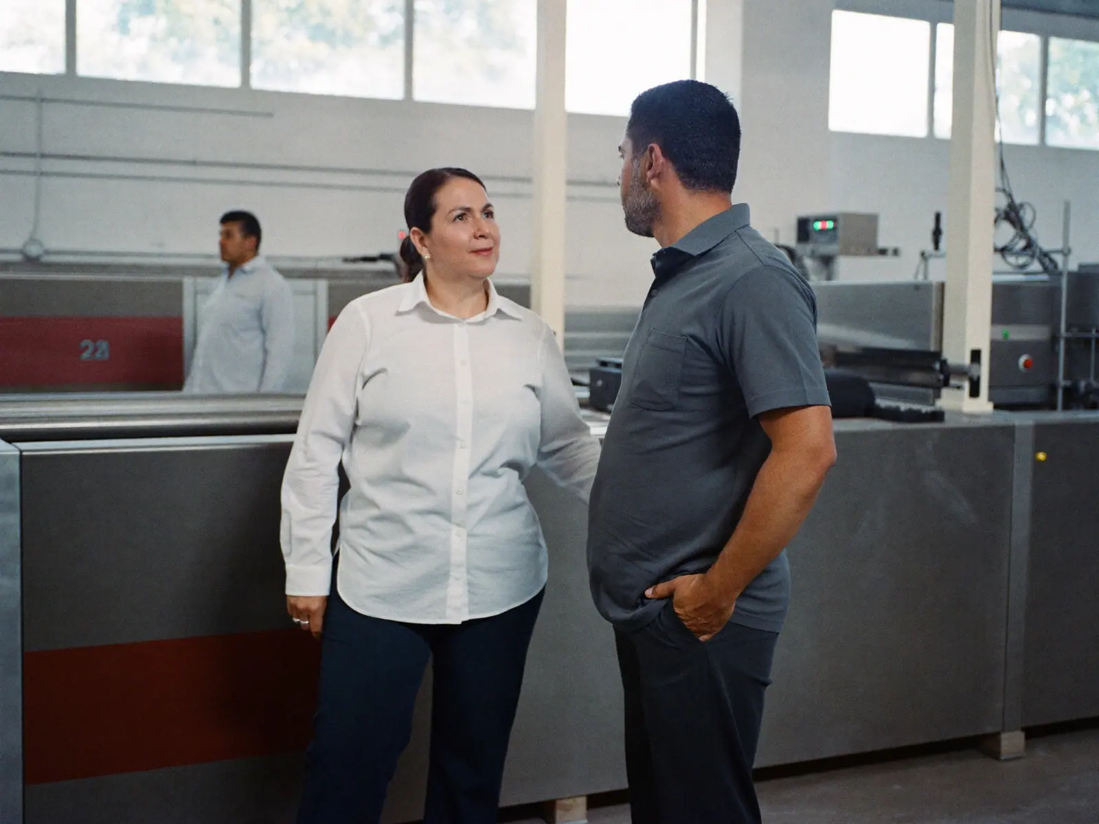 Ingeniera de mantenimiento conversando con un supervisor junto a una línea de producción
